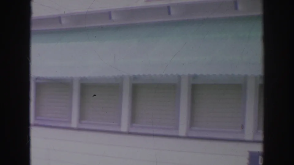 Norfolk 1966 home-movie frame of a house exterior, showing a mint-green awning, shuttered windows, roofline, and soft 8mm film edges.