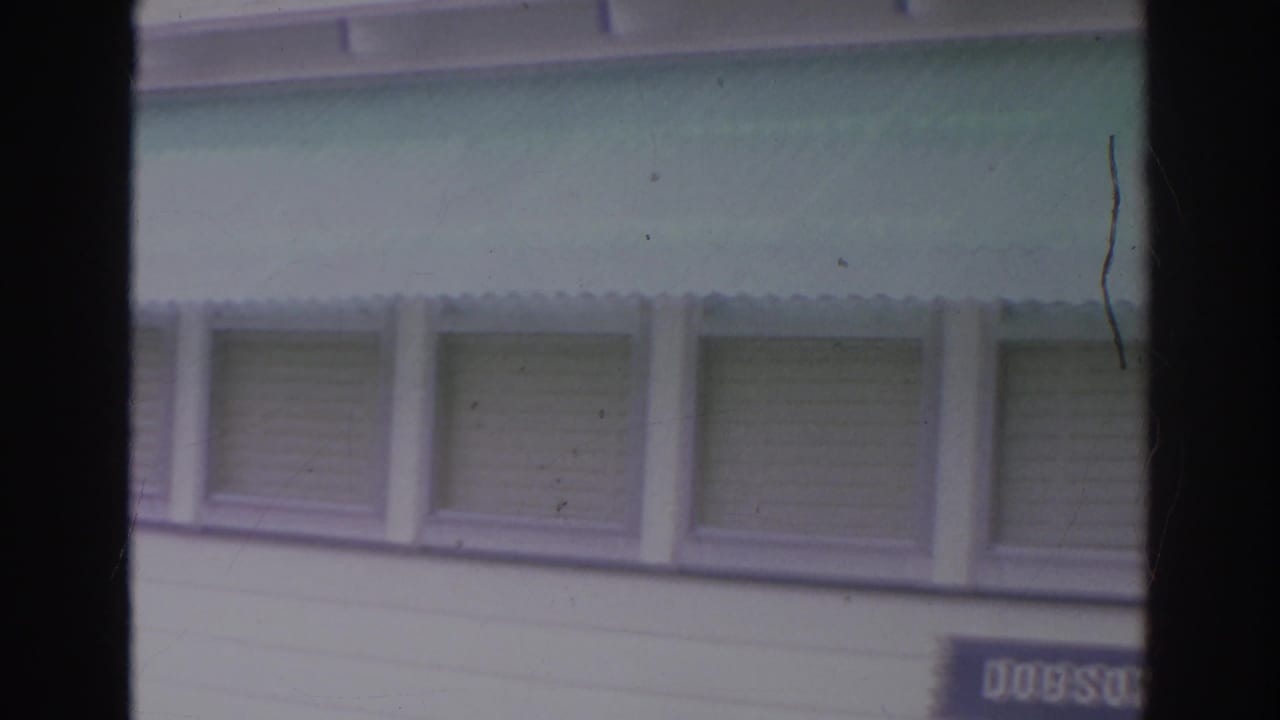 White clapboard facade with green awnings and shuttered windows, partly obscured by film gate edges.