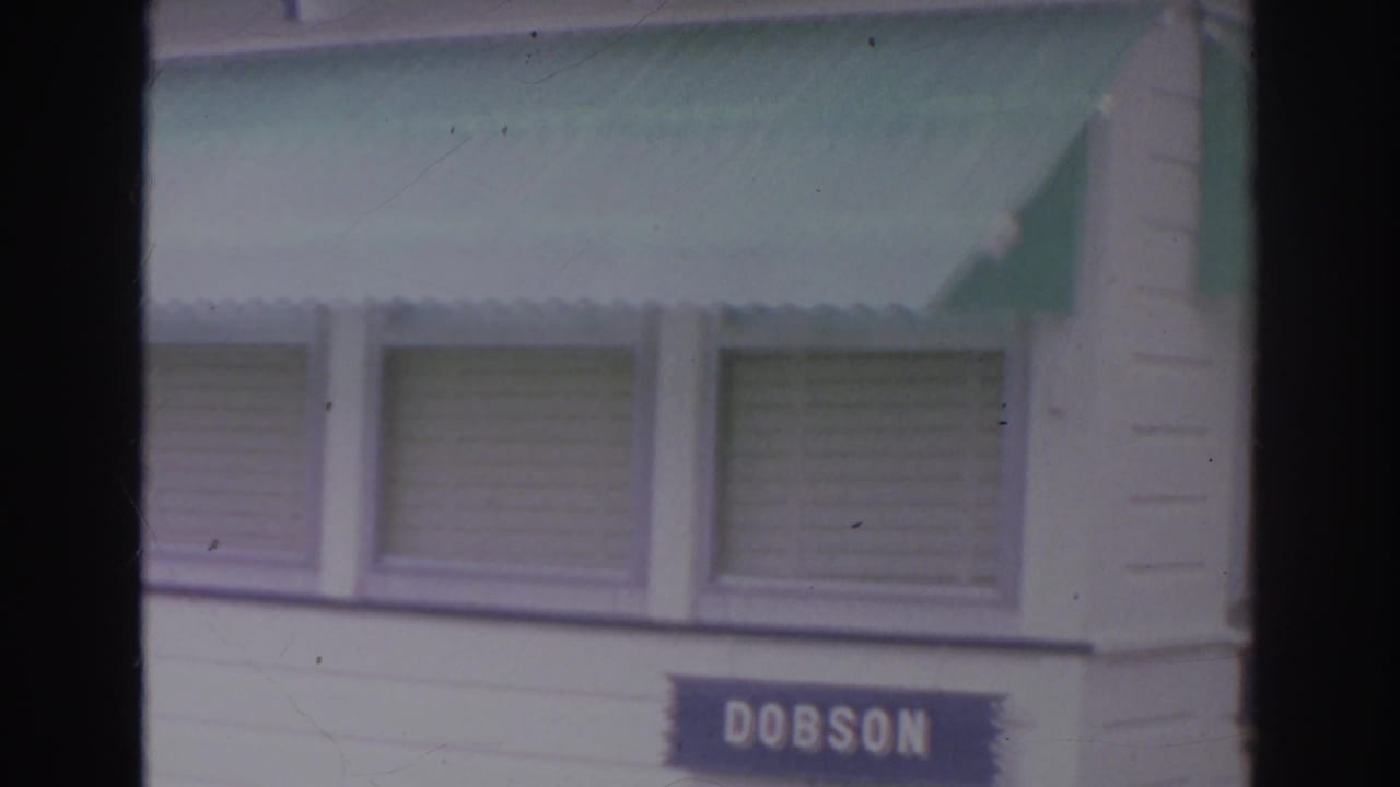 White building exterior with green awnings, shuttered windows, and a blue sign reading DOBSON.