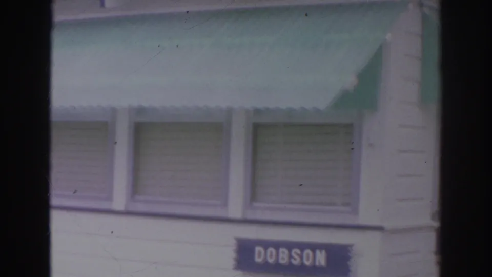 1966 Norfolk home-movie frame with green awnings above windows and a visible blue DOBSON sign on the facade.