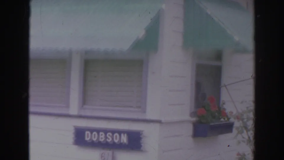1966 Norfolk frame showing the DOBSON sign, green awning, white clapboard wall, and a flower box with red blooms.