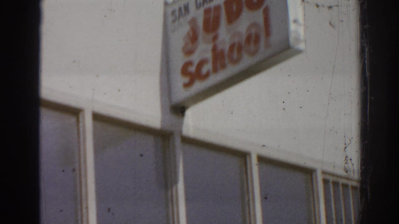 Closer view of the white facade with a red-letter judo school sign and window bays.