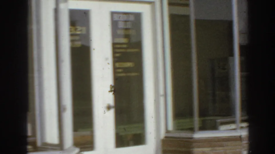 Storefront doorway and tall windows in San Gabriel, with business lettering visible through soft focus and film grain.