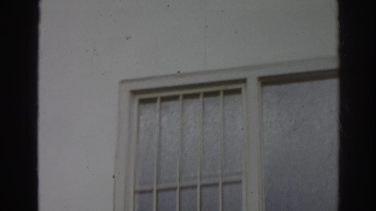 White building exterior with a barred window and dark film-frame edges.