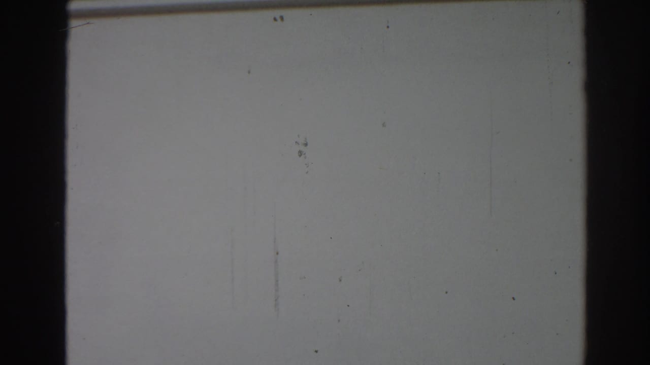 The pan moves across a mostly blank white facade, with a partial window edge and dark 8mm frame border visible.
