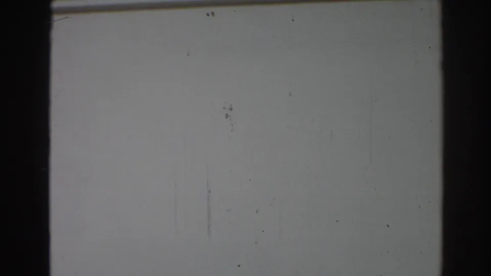 The pan moves across a mostly blank white facade, with a partial window edge and dark 8mm frame border visible.