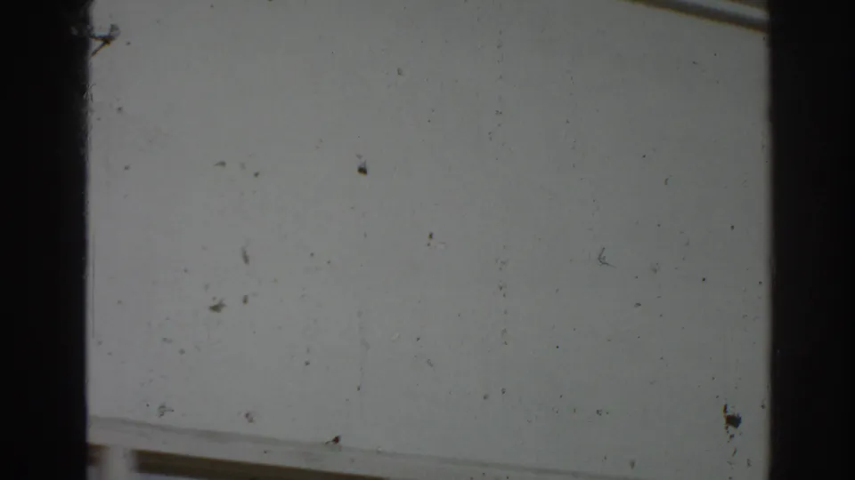 A low portion of the white San Gabriel building exterior shows a partial window and the texture of worn 8mm film.