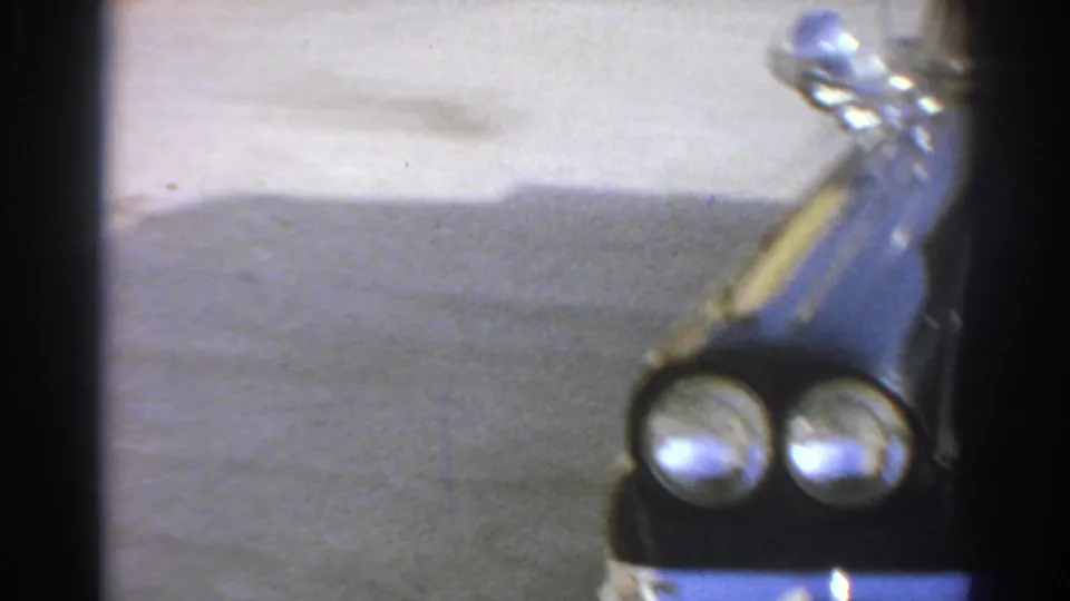 1966 San Gabriel frame showing the black car's front corner, dual headlights, chrome trim, and hood ornament in bright daylight.