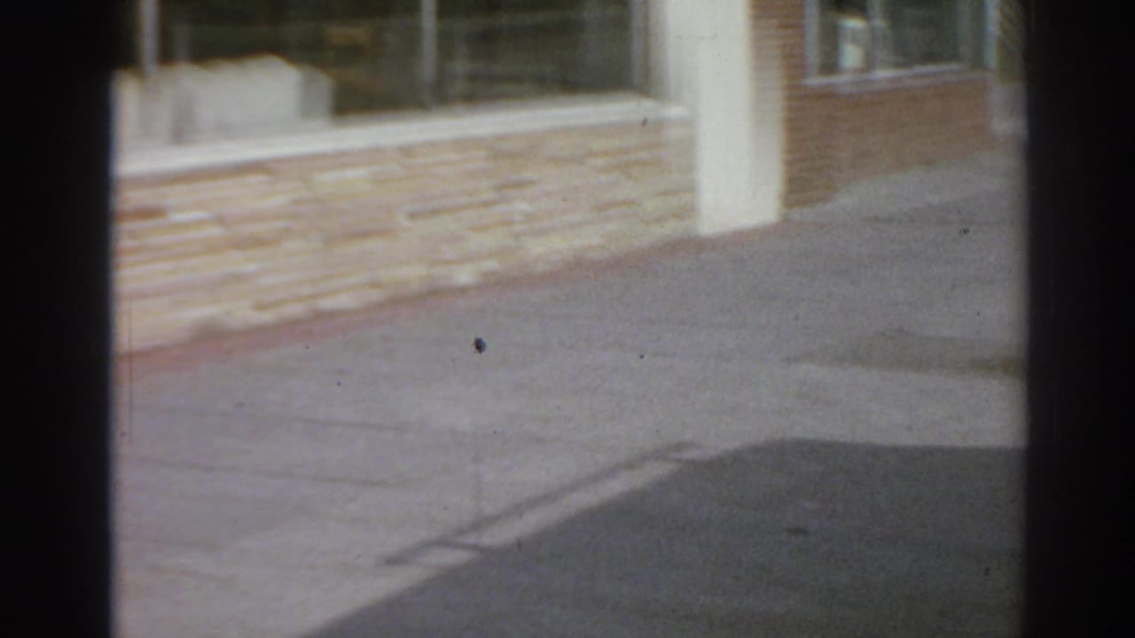 Brick storefront wall, windows, sidewalk, curb, and dark film-frame edge.