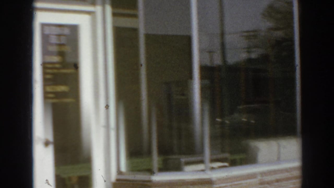 Glass storefront entrance with door, windows, brick base, planter, and dark frame edge.