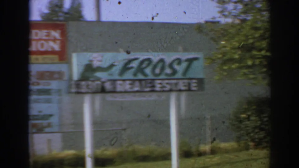 1966 San Gabriel pan frame centered on the Frost Real Estate sign, with Golden Lion signage and trees in the background.