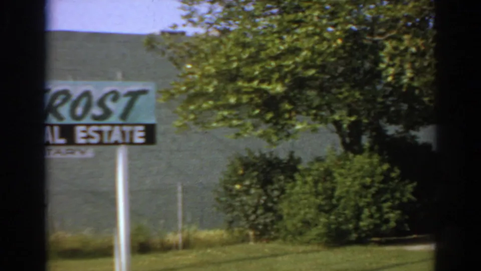 1966 San Gabriel 8mm frame showing part of a Frost Real Estate Notary sign near trees and a building exterior.