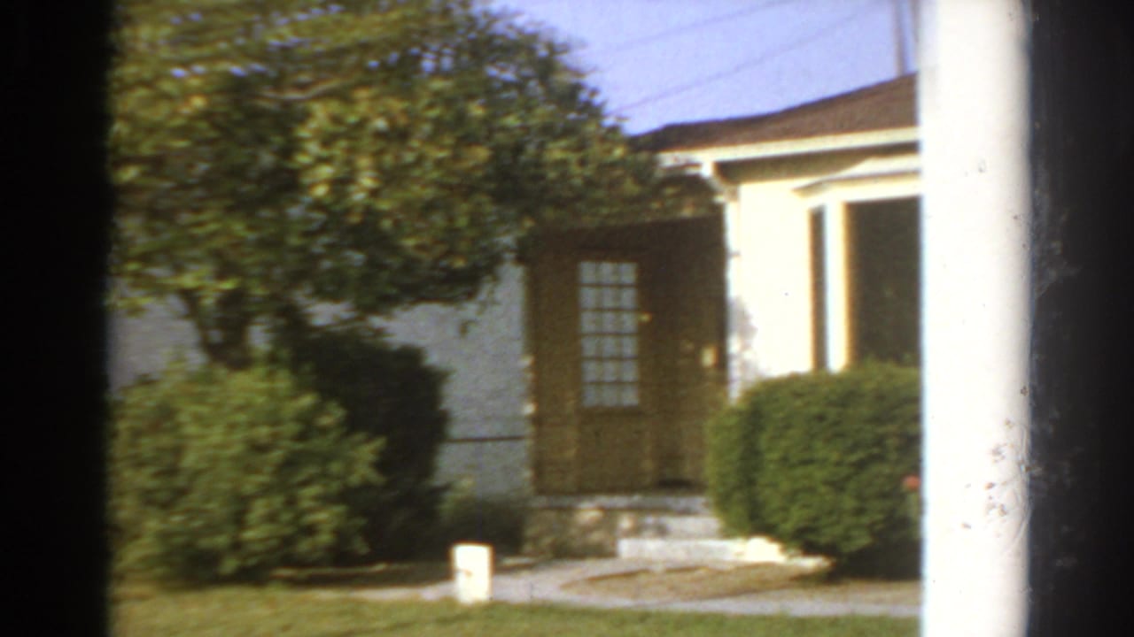1966 San Gabriel residential exterior with trimmed shrubs, a dark doorway, front steps, and a white vertical post.