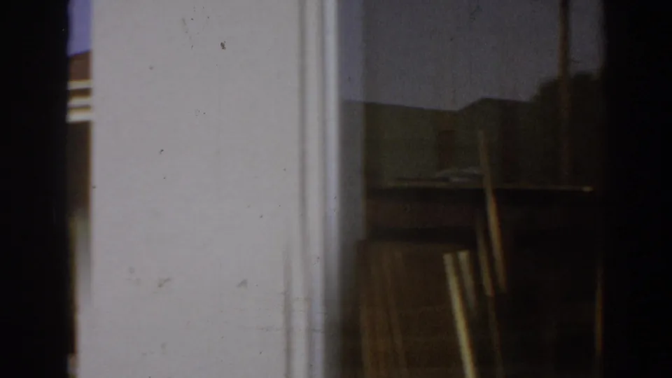 1966 San Gabriel 8mm view into a garage or shed, with a workbench, boards, and soft indoor shadow.