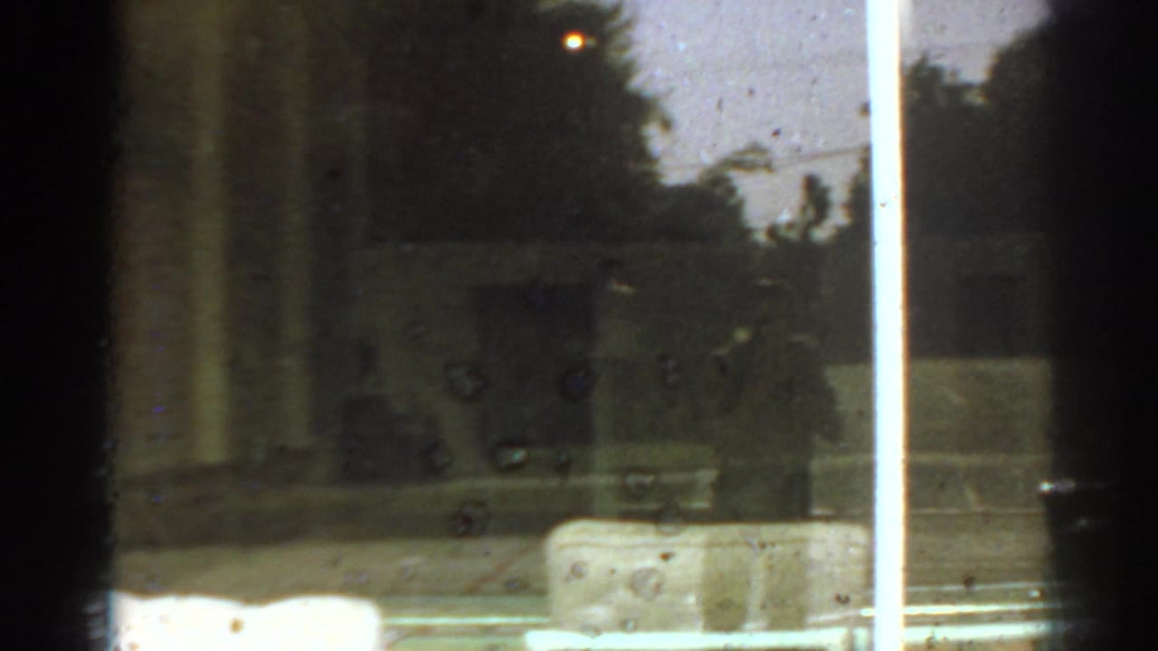 Reflective 8mm view in San Gabriel, California, with dark window bars, outdoor trees, and faint interior shapes.