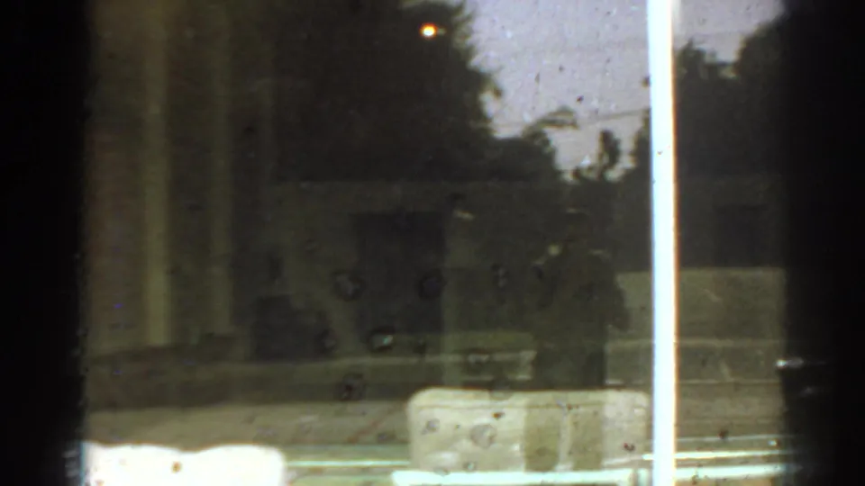 Reflective 8mm view in San Gabriel, California, with dark window bars, outdoor trees, and faint interior shapes.