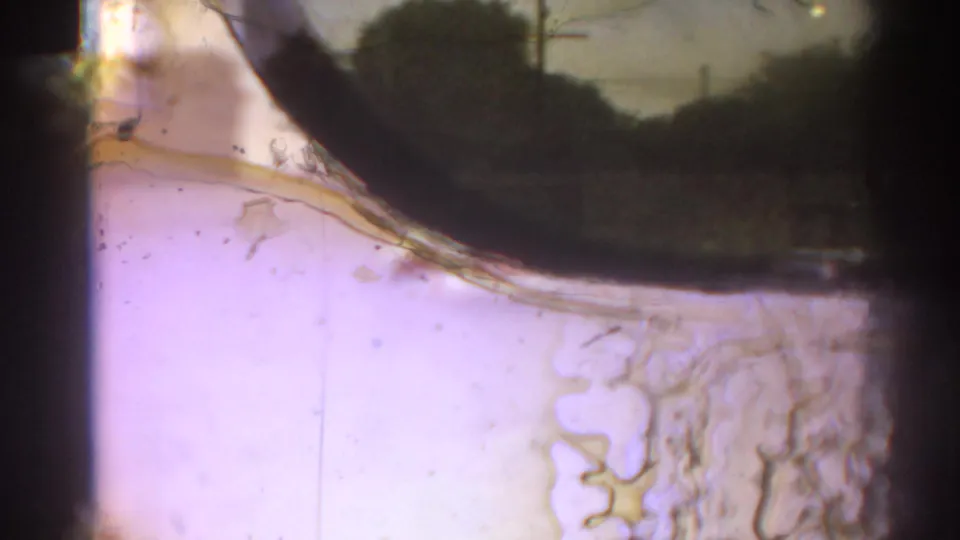 Close 8mm frame dominated by reflective glass, a pale interior surface, dark curved reflection, and visible dust or scratches.