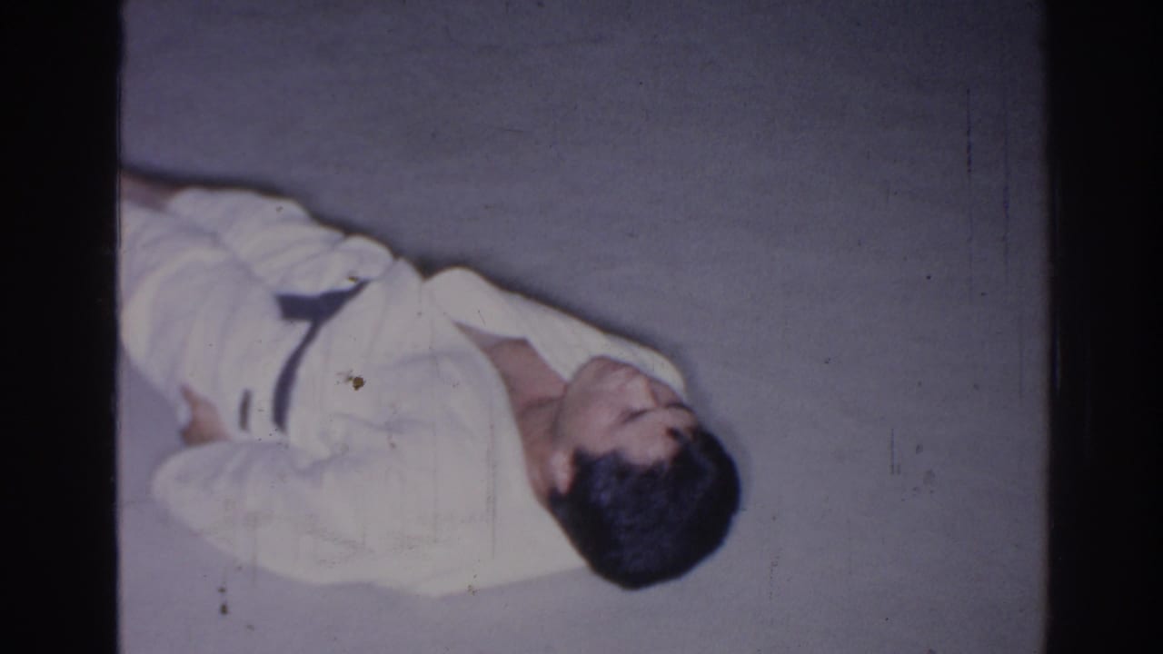 Adult man in a white gi lies on his side on a concrete surface.