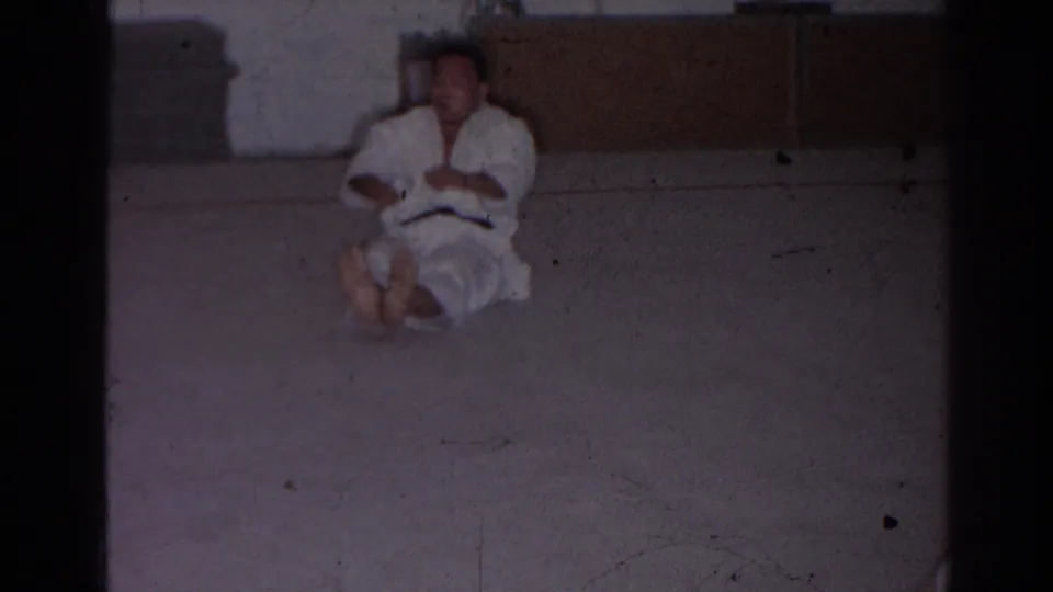 San Gabriel 1966 frame of a martial arts student seated on a padded dojo floor during a home-movie lesson.