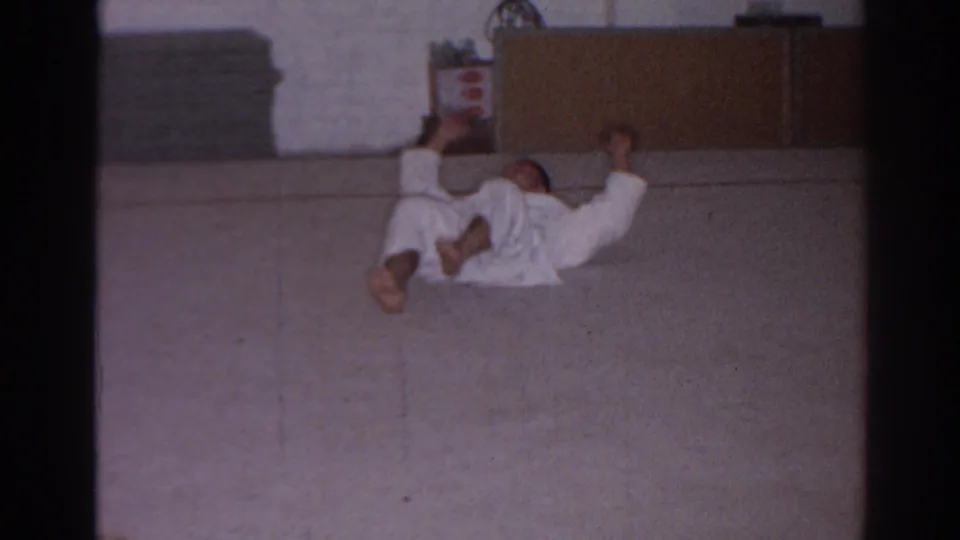 San Gabriel 1966 home-movie frame showing students in white gi practicing floor movements inside a modest dojo.