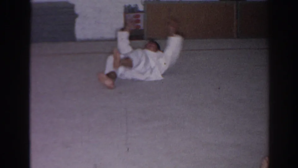 San Gabriel 1966 frame of a martial arts student raising both legs during floor practice in a simple indoor dojo.