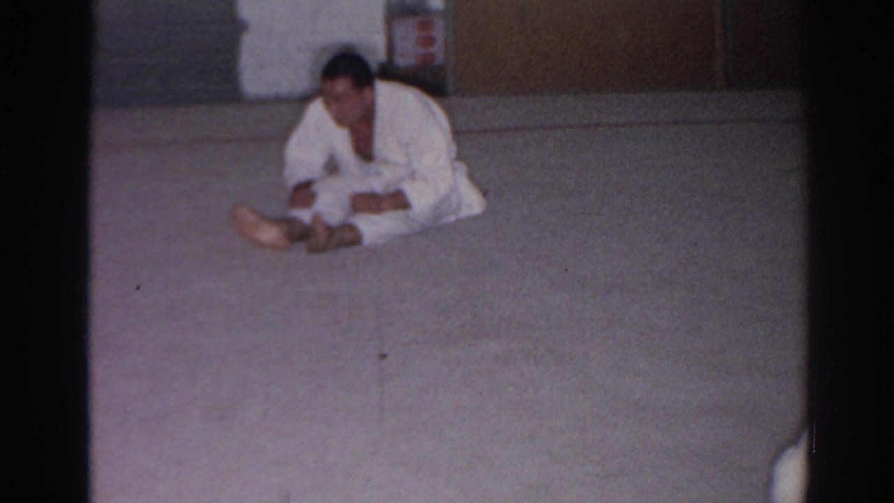 In 1966 San Gabriel footage, a martial arts practitioner in a white gi sits forward on a mat in a simple indoor room.