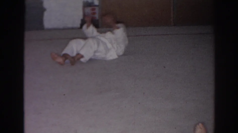 The martial arts practitioner lowers his upper body backward on the mat during the sit-up sequence.