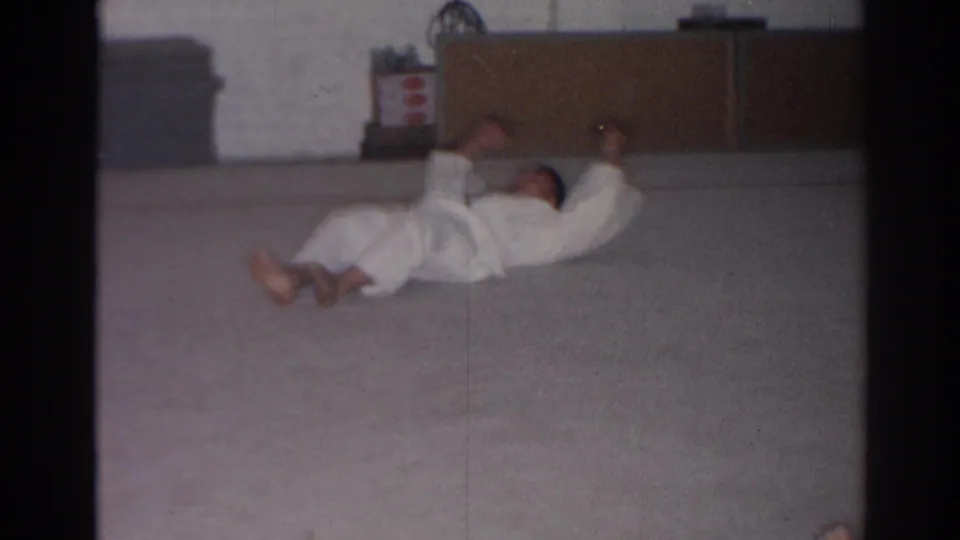 Near the end of the clip, the practitioner lies back on the mat with arms raised in the indoor training room.