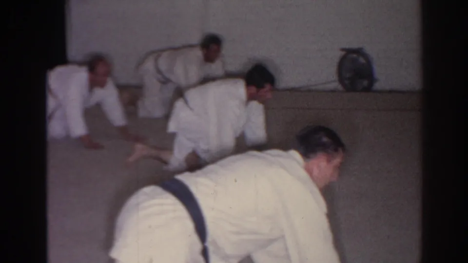 San Gabriel 1966 home-movie frame showing men in white martial arts uniforms crawling or kneeling during a floor exercise.