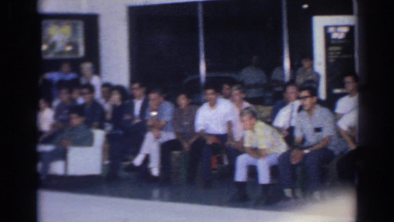 1966 San Gabriel frame with a mixed group of spectators seated in rows along a dark interior wall.