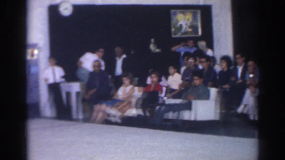 1966 San Gabriel indoor scene with spectators seated near a wall clock and framed decoration during an off-camera event.