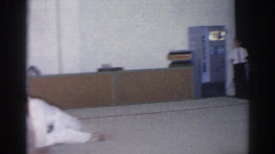 1966 San Gabriel home-movie frame showing an indoor counter and a person standing near a vending machine-like cabinet.