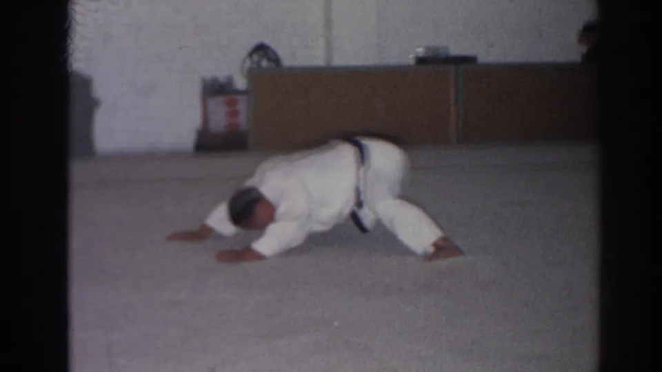 The man lowers his torso close to the mat during a floor exercise in the brief 1966 San Gabriel home-movie gym scene.