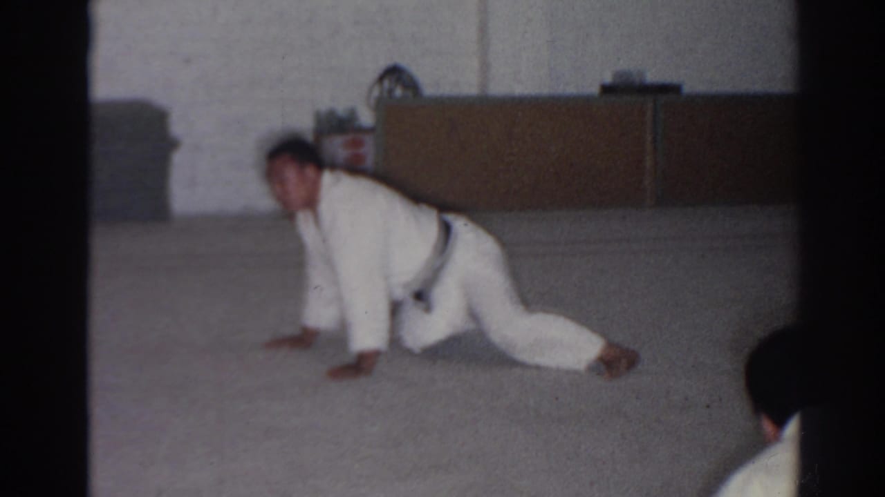 Karate student in a white gi stretches in a low lunge on an indoor floor.