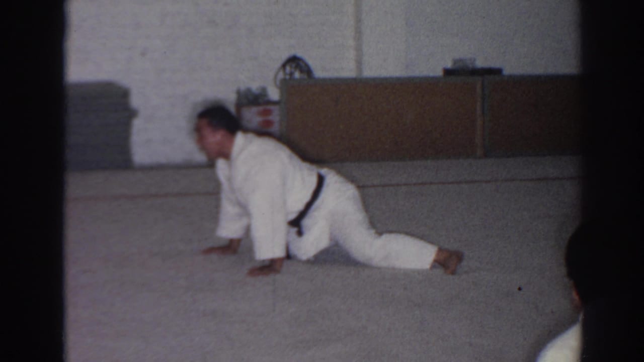 Karate student remains in a floor stretch near storage cabinets and mats.