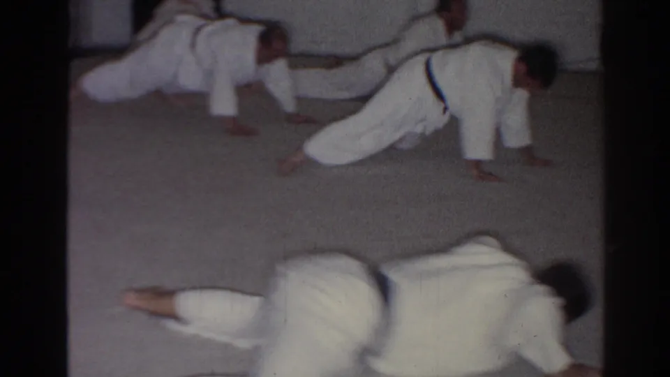 1966 San Gabriel frame showing multiple karate students in white uniforms practicing floor stretches in unison.