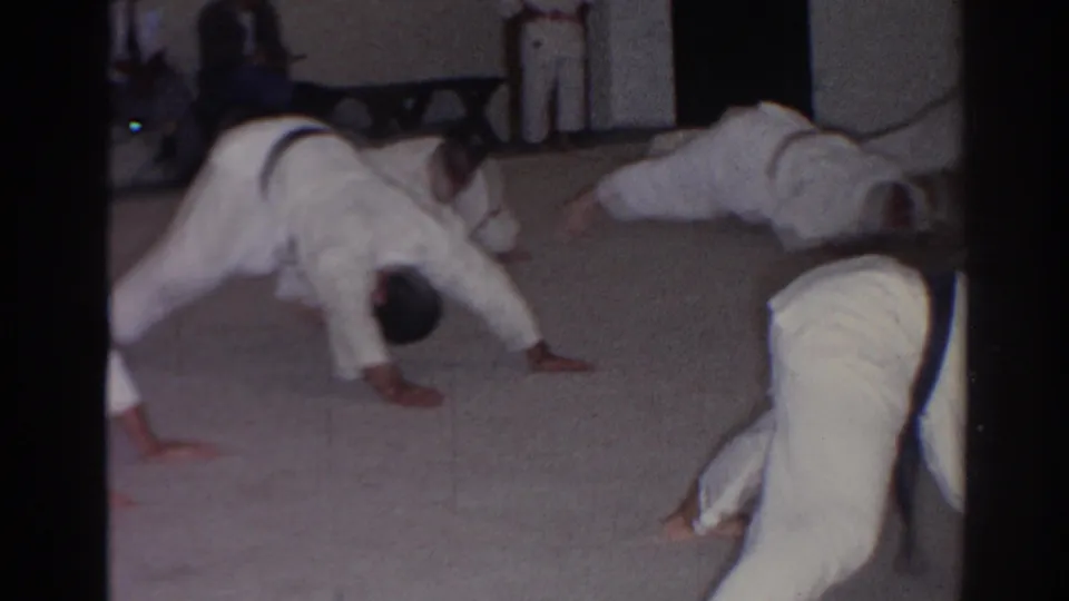 In 1966 San Gabriel, men in white judo gis move through push-ups during an indoor martial arts training session.