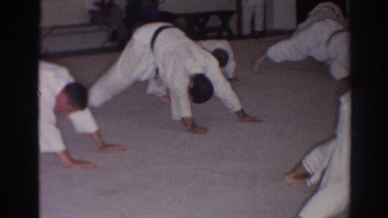 Men in white judo uniforms continue a synchronized push-up drill inside the San Gabriel training room.