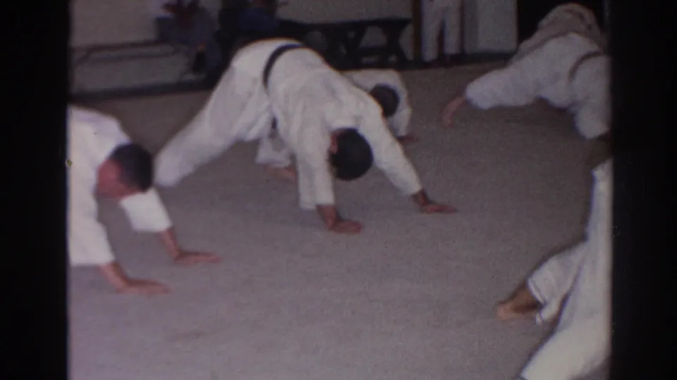 Men in white judo uniforms continue a synchronized push-up drill inside the San Gabriel training room.
