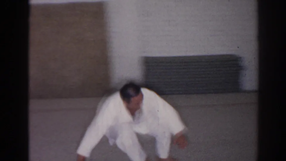 1966 San Gabriel footage shows a martial arts student moving through a low front roll or flip on the dojo floor.