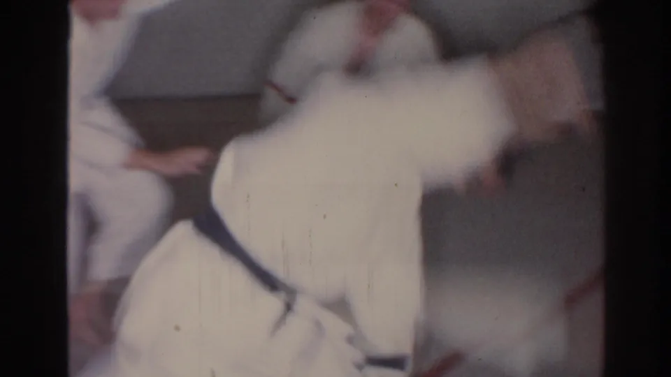 Close, motion-blurred 1966 San Gabriel home-movie frame of martial arts students in white gi during a ground movement.