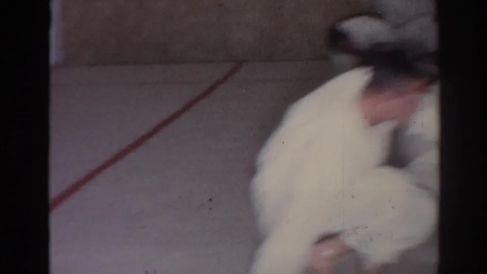 1966 San Gabriel frame showing blurred martial arts movement across a carpeted training floor with a red floor line visible.