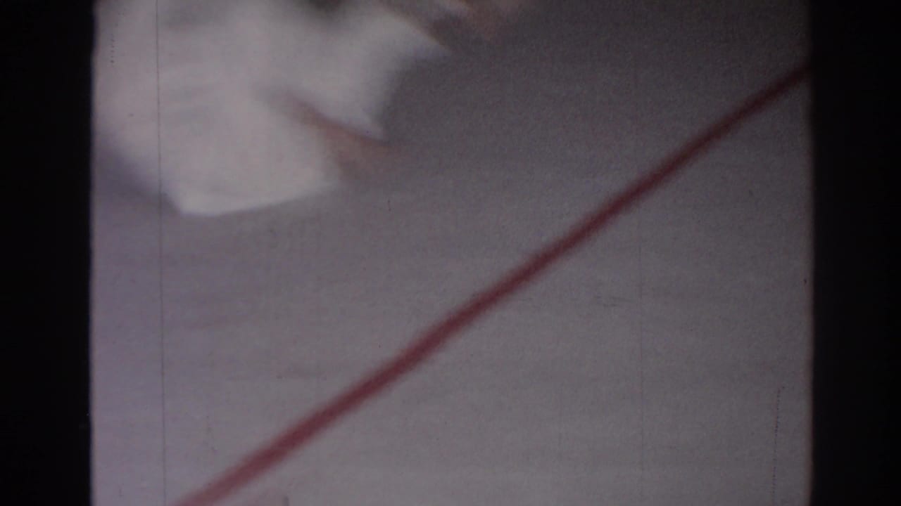 Blurred white gi and red floor line on a mat, framed by dark film edges.