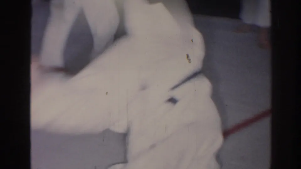 1966 San Gabriel footage shows a male judo practitioner in a white gi and black belt during a ground technique.