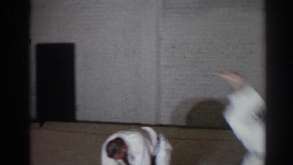 San Gabriel 1966 frame showing a white-uniformed practitioner jumping over a crouched assistant in an indoor dojo.