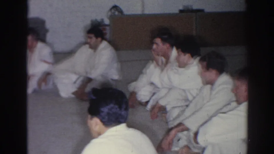 A row of martial arts students in white uniforms sits on a mat during a 1966 San Gabriel dojo lesson.