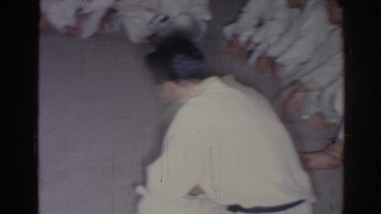 Back view of a person in a white karate uniform near seated participants on a floor.