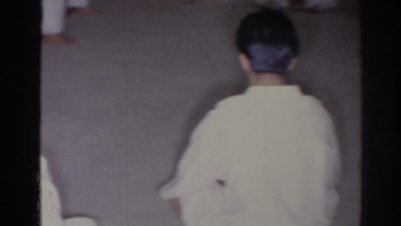 Person in a white uniform seen from behind on a plain floor.