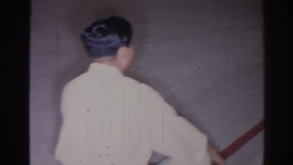 1966 San Gabriel frame with a white-gi practitioner turned partly sideways beside a red diagonal line on the floor.