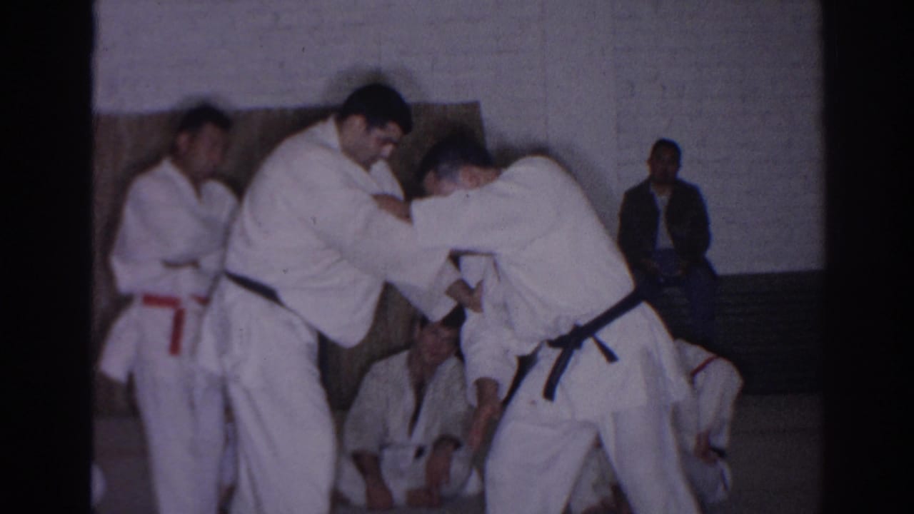 1966 San Gabriel gym scene with two judo practitioners in white gi demonstrating a technique before seated students and onlookers.